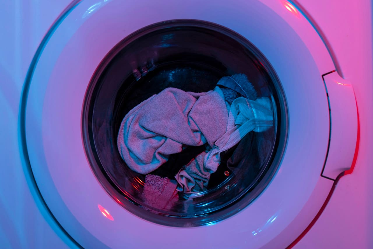 Clothes inside a front-loading washing machine drum, lit in pink and blue