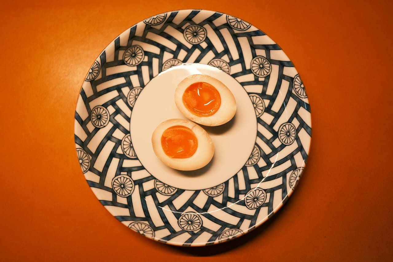 Two halved jammy soft-boiled eggs on a patterned plate